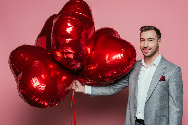 happy man holding red heart balloons for valentines day on pink - Photo, Image