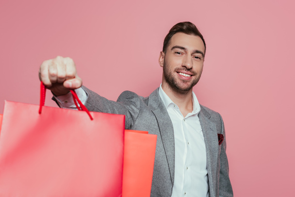 cheerful man holding shopping bags, isolated on pink - Foto, Imagem