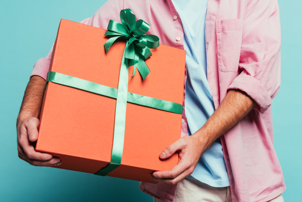 cropped view of man holding big gift box on blue - Foto, afbeelding