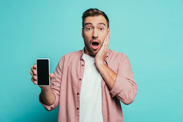 hombre sorprendido mostrando teléfono inteligente con pantalla en blanco, aislado en azul
 - Foto, imagen