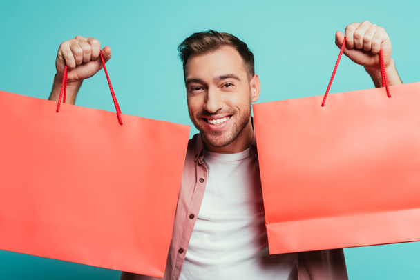 cheerful man holding shopping bags, isolated on blue - Foto, Imagem