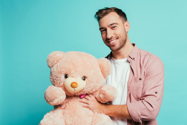 cheerful bearded man holding teddy bear, isolated on blue - Photo, Image