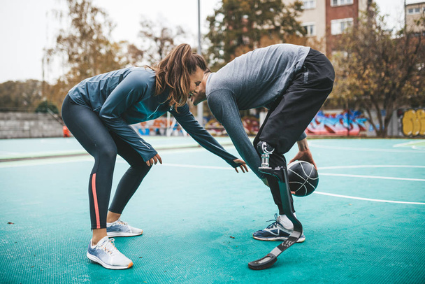Junger Mann mit Beinprothese spielt Basketball mit seinem Freund. - Foto, Bild