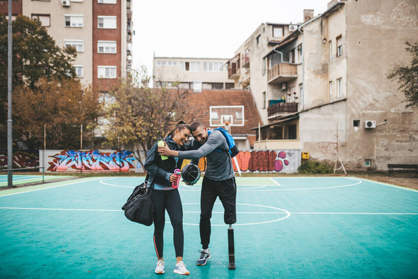 Młody człowiek z protezą nogi zabawia się ze swoim przyjacielem na boisku do koszykówki. - Zdjęcie, obraz