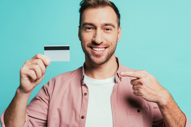 happy bearded man pointing at credit card, isolated on blue - Fotó, kép
