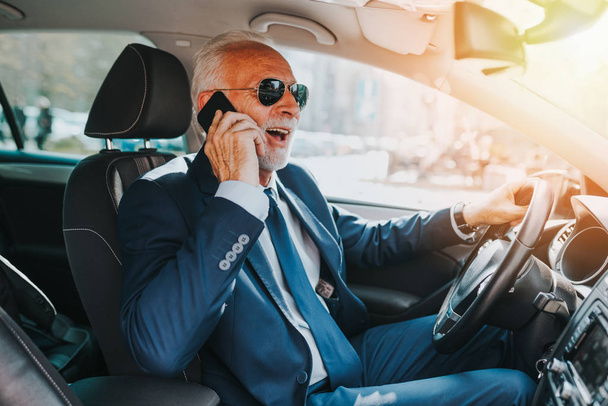 Senior hombre de negocios guapo hablando en el teléfono móvil mientras conduce su coche
 . - Foto, imagen