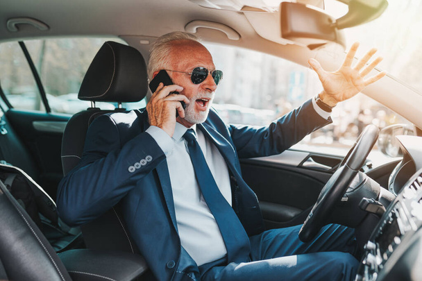 Nervoso anziano di bell'aspetto uomo d'affari arrabbiarsi e nervoso mentre parla sul cellulare e guida la sua auto
. - Foto, immagini