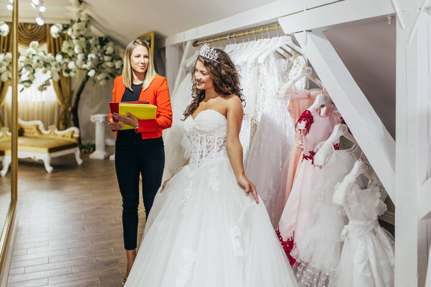 Beautiful young brunette woman choosing wedding dress in a bridal salon. - Fotoğraf, Görsel