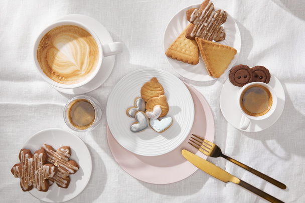Draufsicht auf Kaffee und Kekse auf weißer Tischdecke - Foto, Bild
