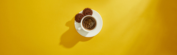 Top view of coffee cup with cookies on saucer on yellow surface, panoramic shot - Valokuva, kuva