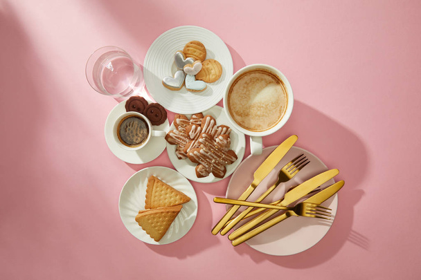 Widok z góry ciasteczka z glazurą, kawa i szklanka wody na różowym tle - Zdjęcie, obraz