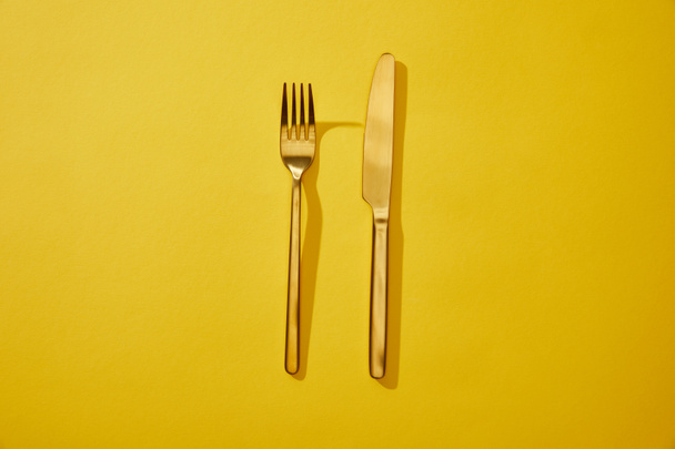 Top view of shiny fork and knife on yellow background with copy space - Photo, Image