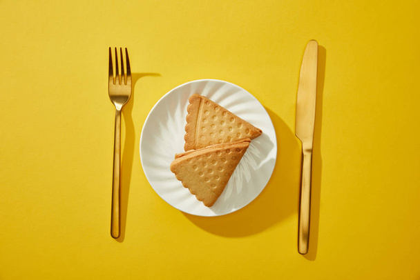 Top view of golden cutlery beside tasty biscuits on plate on yellow background - Фото, зображення