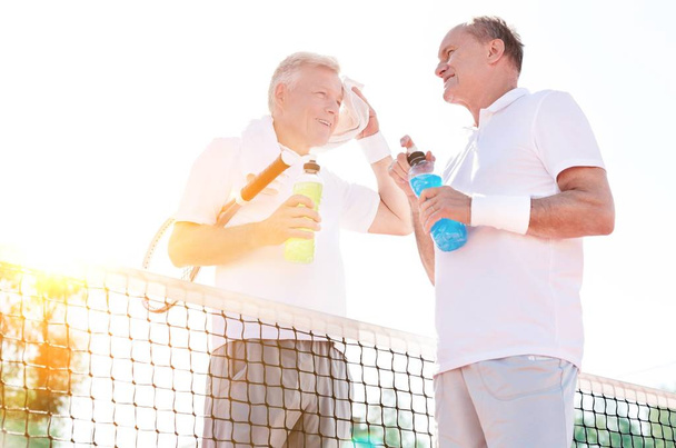 Mature athletes drinking energy drinks in tennis court - Zdjęcie, obraz