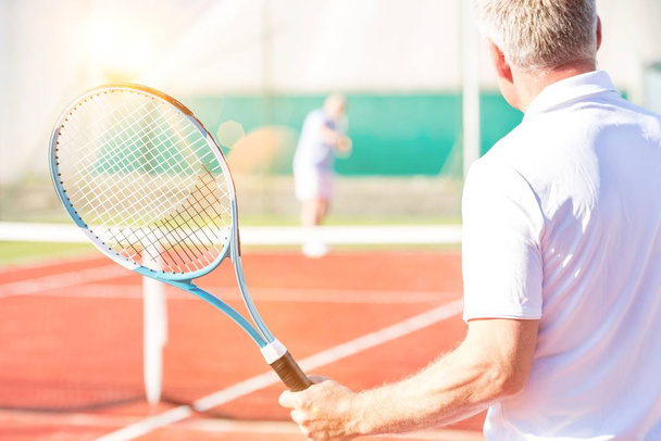 Close up of mature athlete playing tennis in court with yellow lens flare in background  - Foto, immagini