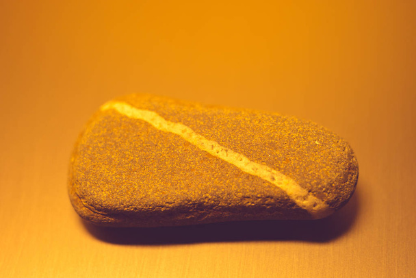 Piedra de guijarro con línea blanca diagonal natural sobre la mesa, luz naranja
. - Foto, imagen