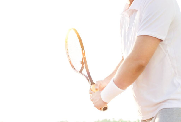 Mature tennis athlete hitting ball with racket in court with yellow lens flare  - Fotoğraf, Görsel