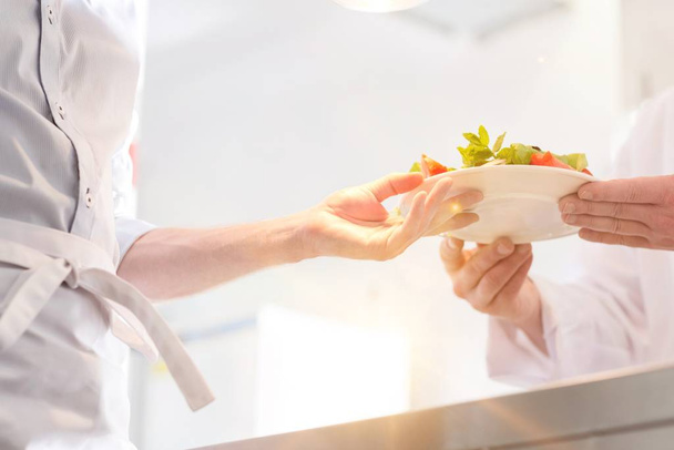 Chef giving salad to waiter to be served for the customer in kitchen - Valokuva, kuva