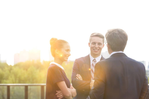 Business people discussing plans before meeting in office rooftop with yellow lens flare in background  - Фото, изображение