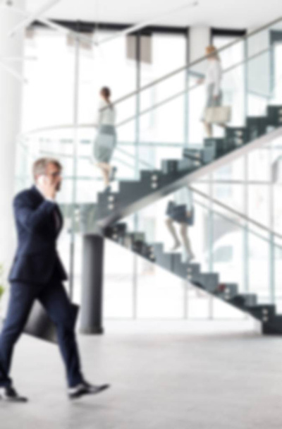 Mature businessman walking while talking at office against staircase - Photo, image