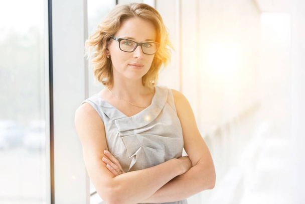 Portrait of confident businesswoman standing with arms crossed and yellow lens flare in background - Fotoğraf, Görsel