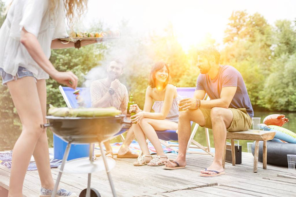Nő grillezés élelmiszer, míg a piknik a barátaival a mólón tó - Fotó, kép