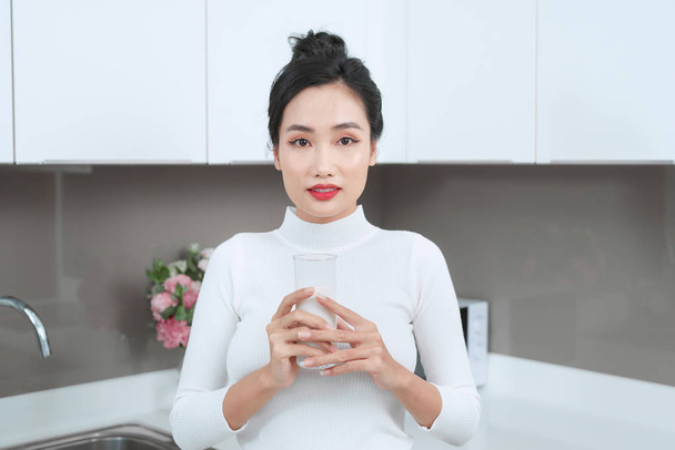 Portrait of young Asian woman drinking milk in the kitchen.  - Foto, afbeelding