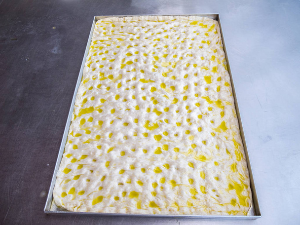 Een dienblad van focaccia Genovese voor het bakken, focaccia is een platte oven gebakken Italiaans brood product, traditioneel recept uit Ligurië regio, vergelijkbaar in stijl en textuur als pizza deeg - Foto, afbeelding