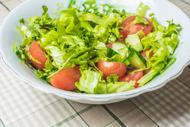 Tuore vihreä salaatti tomaattia ja kurkkua lautasella keittiön pöydällä. - Valokuva, kuva