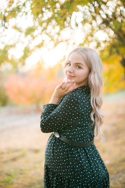 Cute pregnant woman with blond hair walks in the autumn park at sunset. Happy motherhood. Autumn pregnancy - Fotó, kép