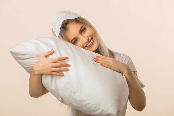 beautiful young woman in a sleep mask on a beige background with a pillow in her hands - Fotografie, Obrázek