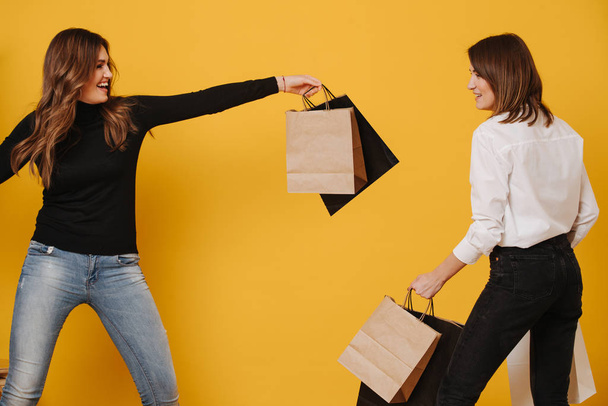 Two happy female friends happy and uplifting after shopping over yellow - 写真・画像