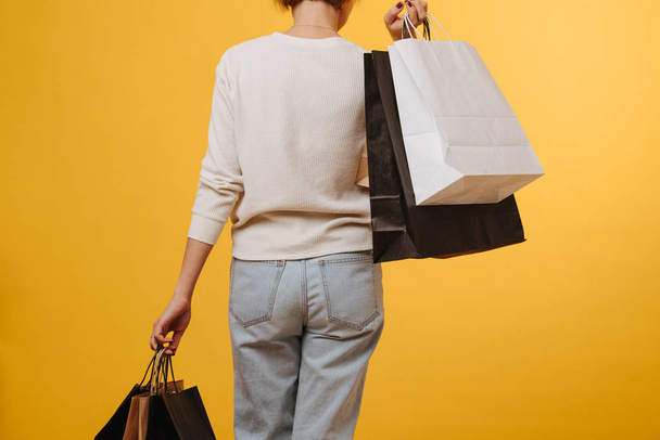 Woman in old loose comfortable jeans carrying bunch of shopping paper bags - Фото, изображение