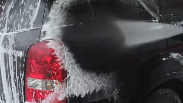 Un uomo lava un'auto nera. Video al rallentatore di un processo di lavaggio auto in un autolavaggio self-service. Un getto d'acqua con una lavata ad alta pressione dalla sporcizia dall'auto. Vista laterale. Drenaggi detergenti schiumosi
 - Filmati, video