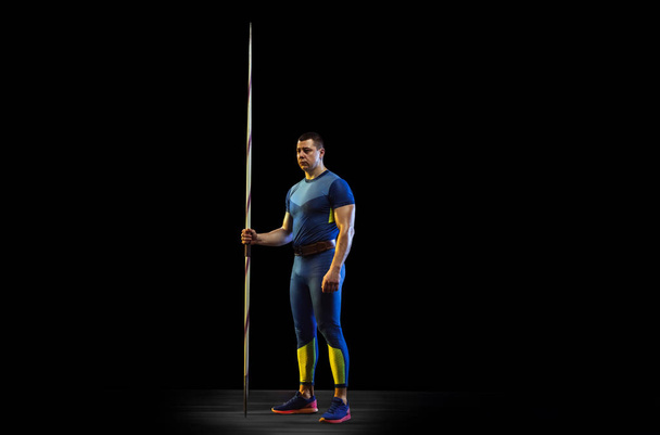 Male athlete practicing in throwing javelin isolated on black studio background in neon light - Foto, Bild