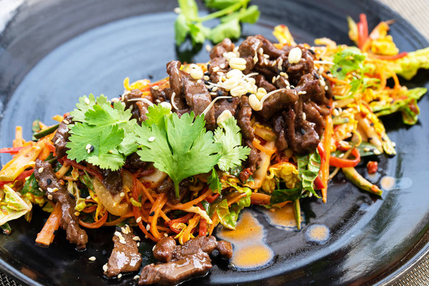traditionelles koreanisches Essen - frischer Rindfleischsalat auf dem schwarzen Teller. - Foto, Bild