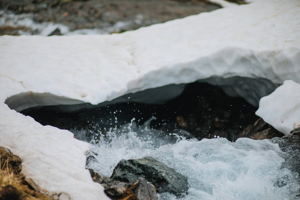 Yksityiskohtainen katsaus veteen kulkee jään alla joessa. Lumi sulaa vuorilta ja virtaa purossa, lähellä
. - Valokuva, kuva