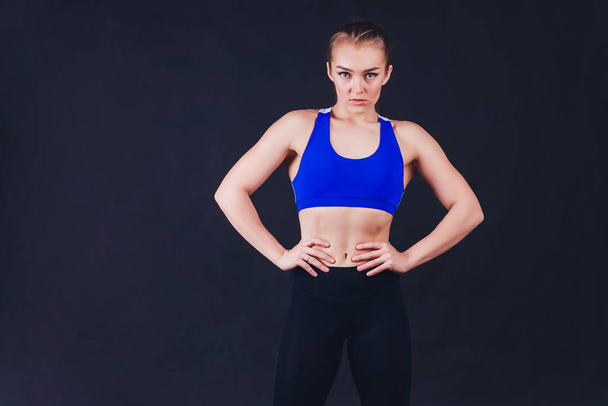 Young fitness woman with gloved hands featuring tight abdominal muscles over black background with copy space Muscular single fit woman with long blonde hair and abs Fitness people training. - Photo, image