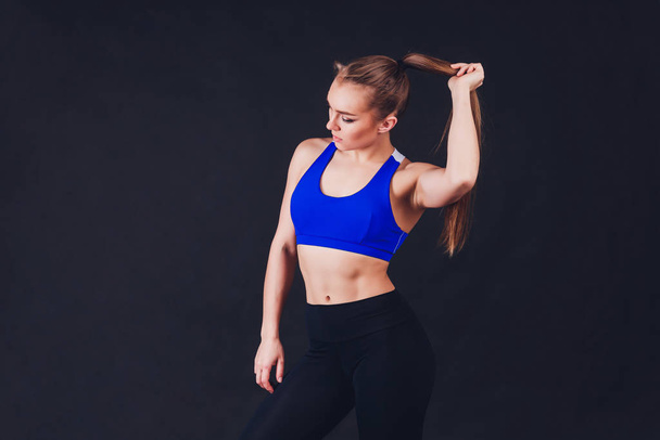 Young fitness woman with gloved hands featuring tight abdominal muscles over black background with copy space Muscular single fit woman with long blonde hair and abs Fitness people training. - Foto, imagen