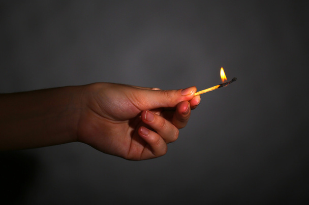 Burning match in hand on black background - Foto, afbeelding
