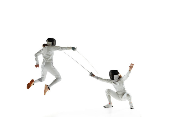 Teen girls in fencing costumes with swords in hands isolated on white background - 写真・画像