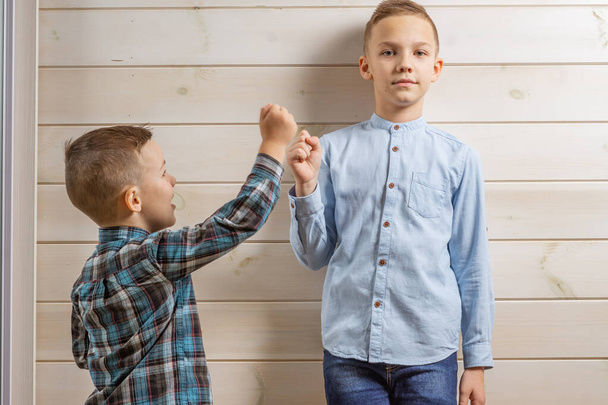Egy négyéves fiú kék klepy ingben könnyes fából készült háttéren sír, és a tízéves öccse áll és kő-papír-ollót játszik.. - Fotó, kép