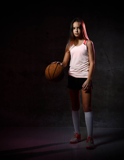 Beautiful caucasian teen woman in sportswear playing basketball . Sport concept isolated on black background. - Foto, immagini