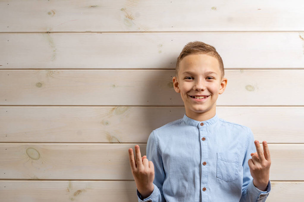 A boy of 10 years old in a blue shirt smiles on a light wooden b - Fotoğraf, Görsel