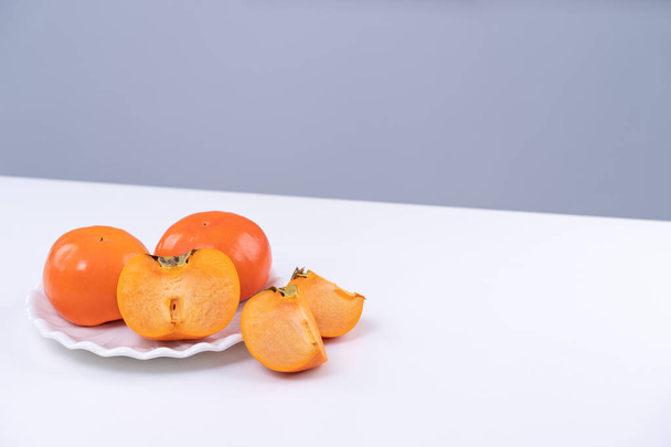 Fresh beautiful sliced sweet persimmon kaki isolated on white kitchen table with gray blue background, Chinese lunar new year design concept, close up. - Photo, image