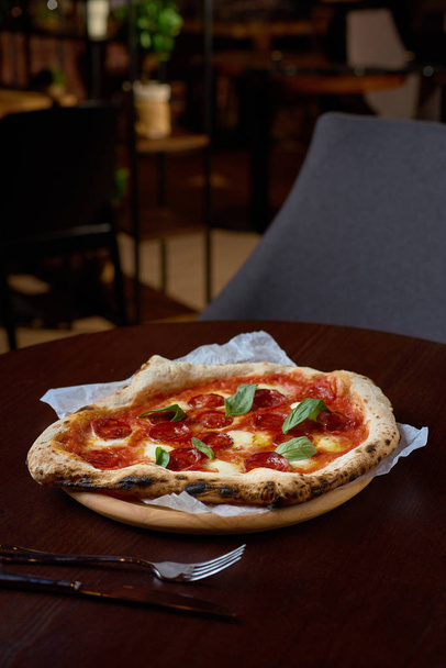Food concept. Fresh original Italian pizza on a wooden board in Italian pizzeria or restaurant. - Fotoğraf, Görsel