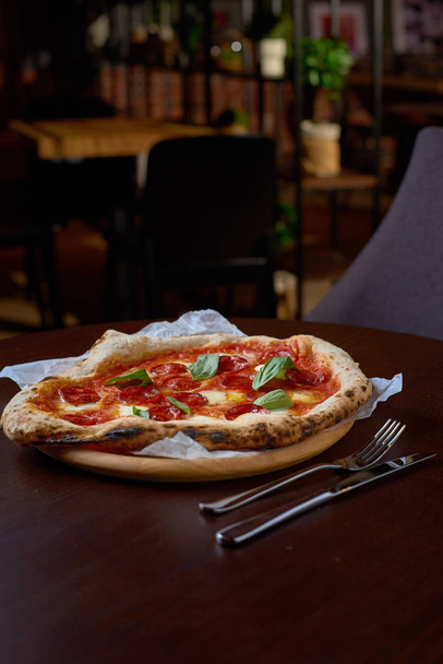Food concept. Fresh original Italian pizza on a wooden board in Italian pizzeria or restaurant. - Fotoğraf, Görsel