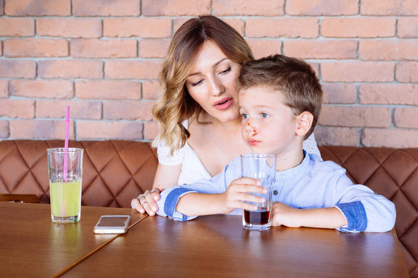 Boy drinking soda soft drink in the cafe with his mom. Unhealthy children habits - Фото, зображення