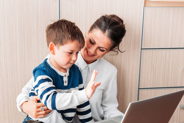 Young mom and her son, sitting on the floor looking at laptop and waving. - Valokuva, kuva