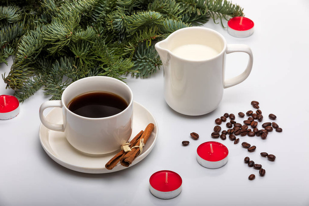 Cup of espresso with milk, cinnomon sticks, fir trees, red candles and on a white background. - 写真・画像